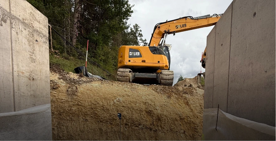 Ein gelber Liebherr Raupenbagger arbeitet auf einer Baustelle und bewegt Erde für den Tiefbau. Fachleute überwachen die Arbeiten und prüfen die Verdichtung des Bodens.