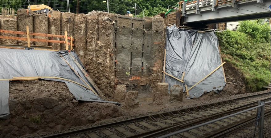 Bauarbeiten an einer Bahnstrecke mit Erdbewegungen, Maschinen und neuen Brücken verbessern den Zugverkehr und die Infrastruktur.