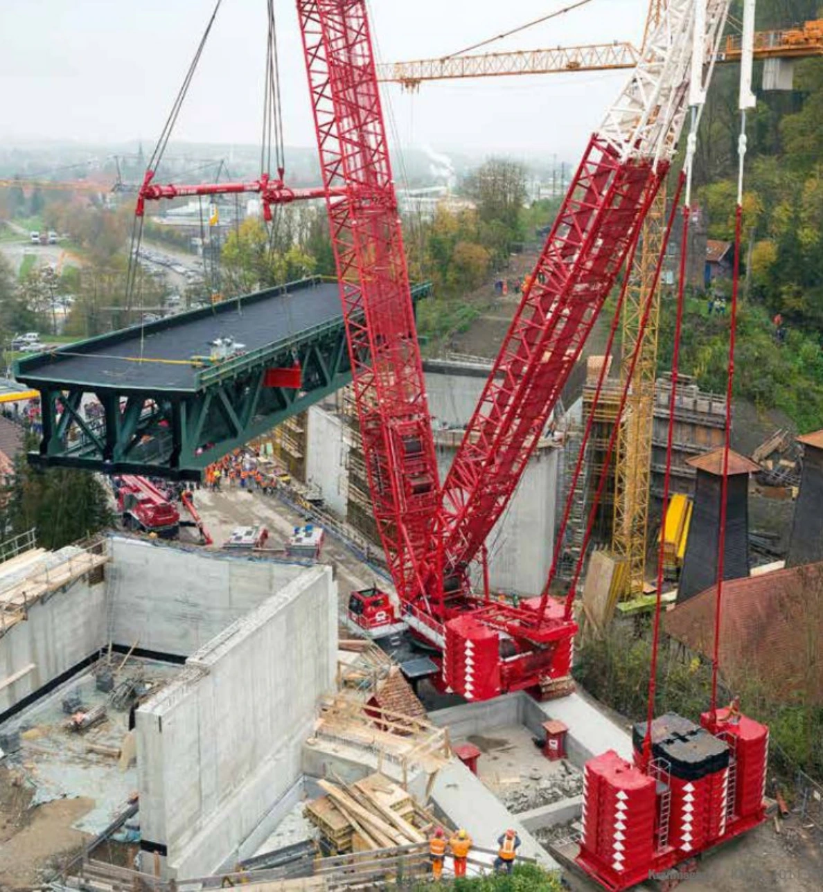 Großer Liebherr Raupenkran hebt ein Brückenteil auf einer Baustelle an. Der Kran wird beim Neubau einer Eisenbahnüberführung eingesetzt.