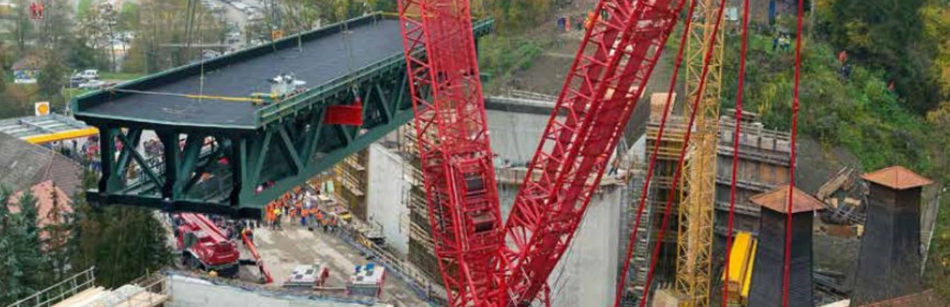 Großer Liebherr Raupenkran hebt ein Brückenteil auf einer Baustelle an. Der Kran wird beim Neubau einer Eisenbahnüberführung eingesetzt.