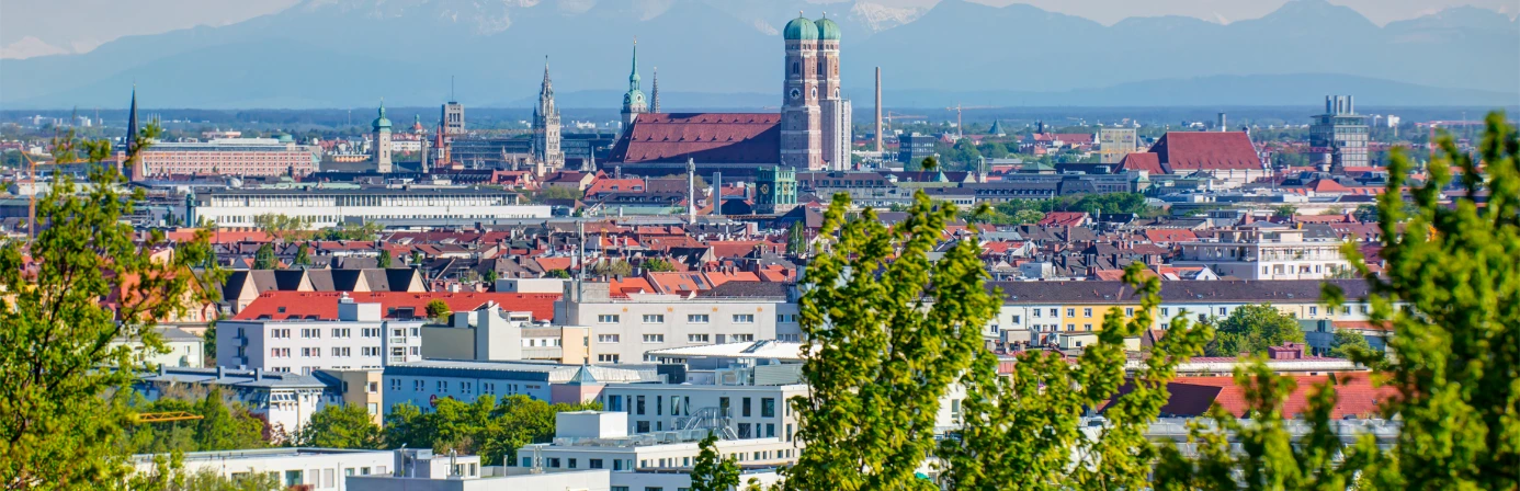 Panorama der Münchner Altstadt mit der Frauenkirche und Blick auf die Alpen an einem klaren Tag.