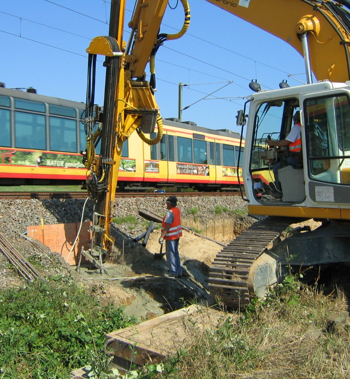 Baustelle an einer Bahnstrecke mit Bagger und Bohrgerät bei Gründungsarbeiten. Die Maßnahme dient der Erneuerung der Schieneninfrastruktur.
