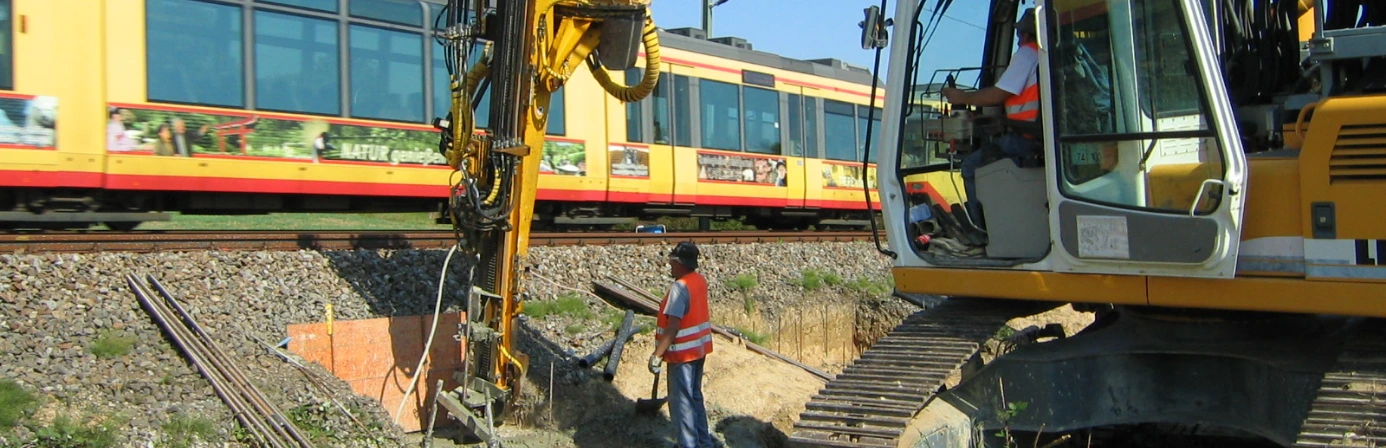 Baustelle an einer Bahnstrecke mit Bagger und Bohrgerät bei Gründungsarbeiten. Die Maßnahme dient der Erneuerung der Schieneninfrastruktur.